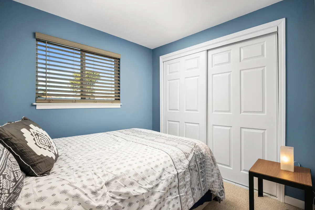A tranquil bedroom with a neatly made bed, a window allowing in sunlight, and a simple nightstand. The uncluttered space is inviting and ideal for relaxation and restful sleep, capturing the essence of a cozy guest room.