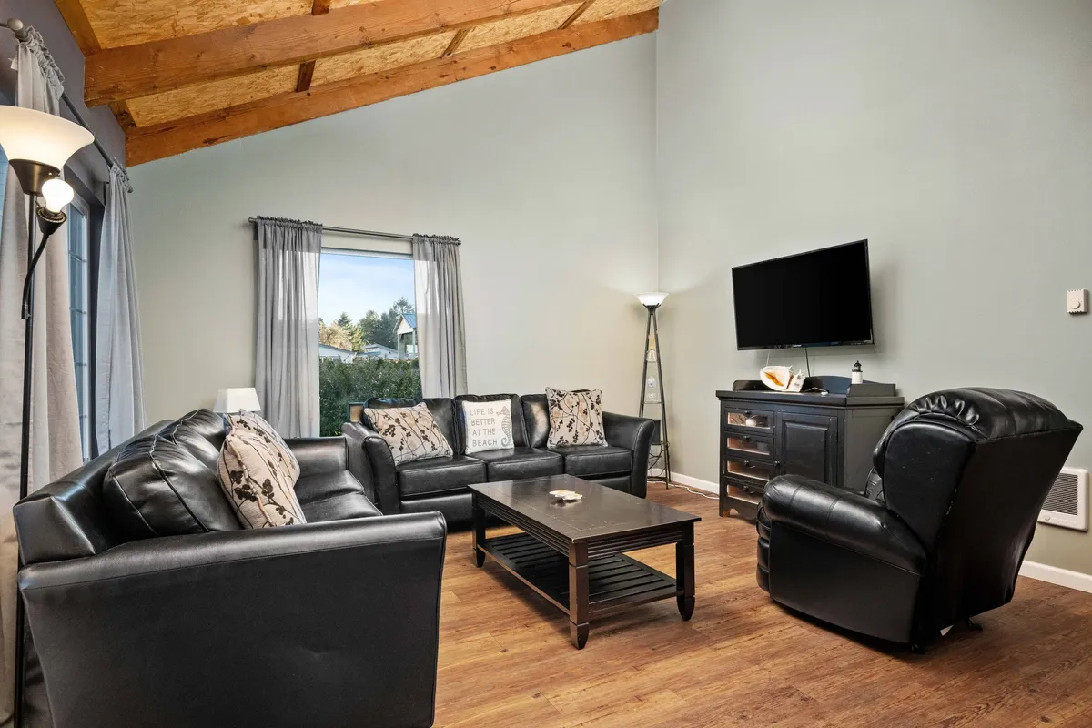 This image captures the main living area featuring plush leather sofas arranged around a coffee table, with a large window letting in ample sunlight. The cozy setup is perfect for relaxing, socializing, watching TV, or gathering for board games.