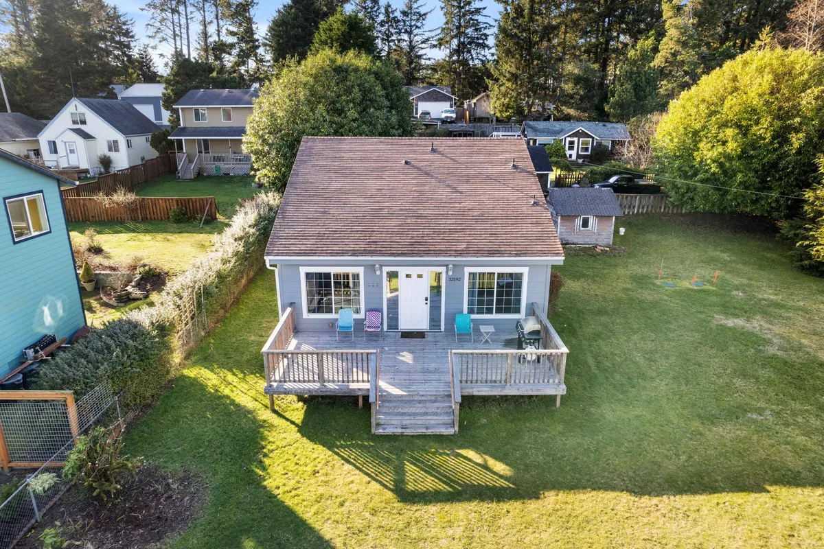 A cozy exterior shot showing a deck with comfortable chairs and a front porch surrounded by lush greenery. The inviting setup encourages relaxing with morning coffee or gathering with friends and family while enjoying nature.