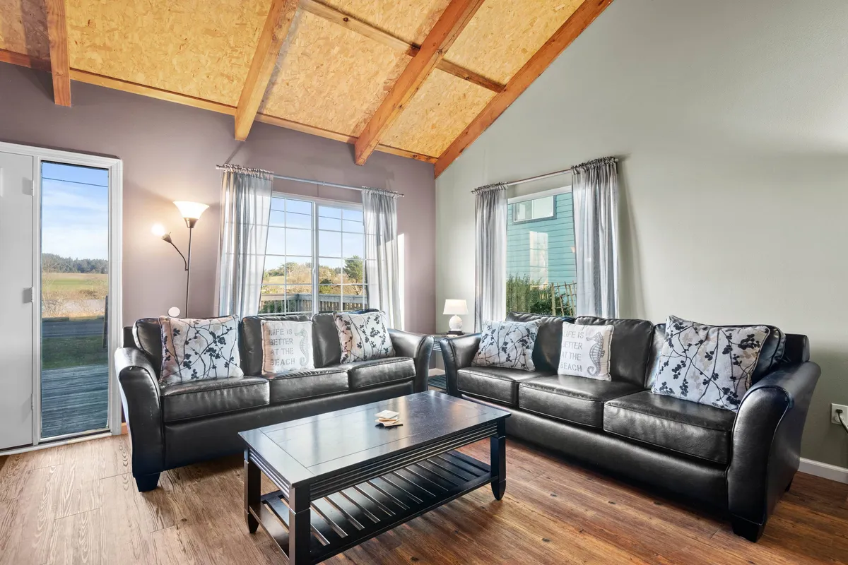 A warmly lit living space featuring plush sofas arranged for conversation, a coffee table perfect for board games or sharing snacks, and large windows that let in sunset light. The arrangement invites relaxation, socializing, and downtime with family.