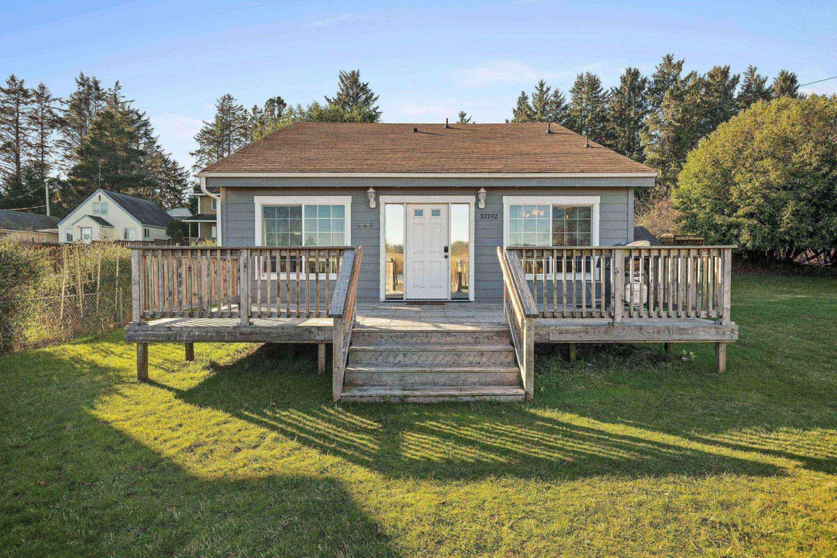 The exterior of the property features a wooden deck, front door, and large windows, with seating perfect for enjoying the outdoors. The deck is surrounded by greenery, inviting guests to relax with a morning coffee or unwind after a day of exploring.