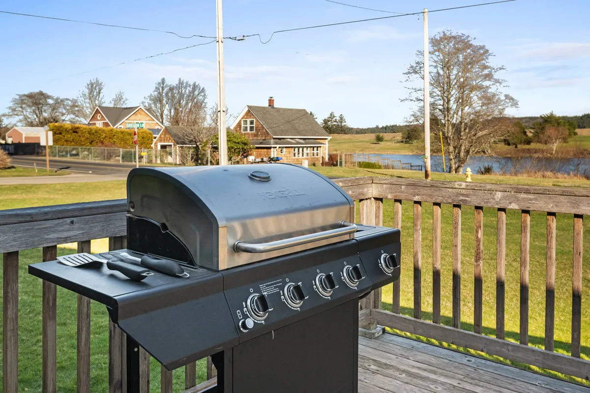 The exterior scene showcases a grill, landscaped pond, and a view of the houses, creating a cheerful setting for barbecuing, outdoor dining, and peaceful mornings. Colorful chairs and open space invite group participation and relaxation.