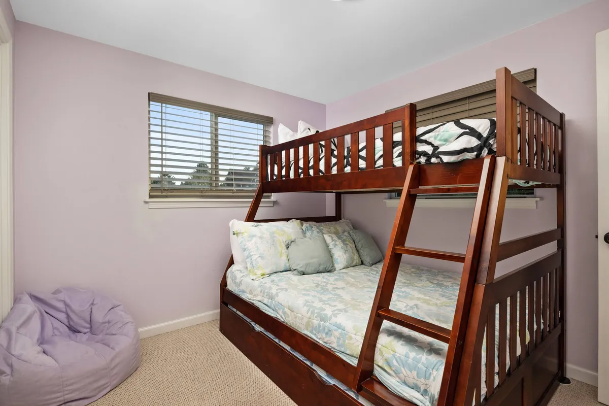 A playful bunk room with a twin-over-full bunk bed and a cozy bean bag chair near a window. Natural light streams in, highlighting the space's fun, kid-friendly ambiance—perfect for children, cousins, or friends looking for a comfortable place to unwind and play.