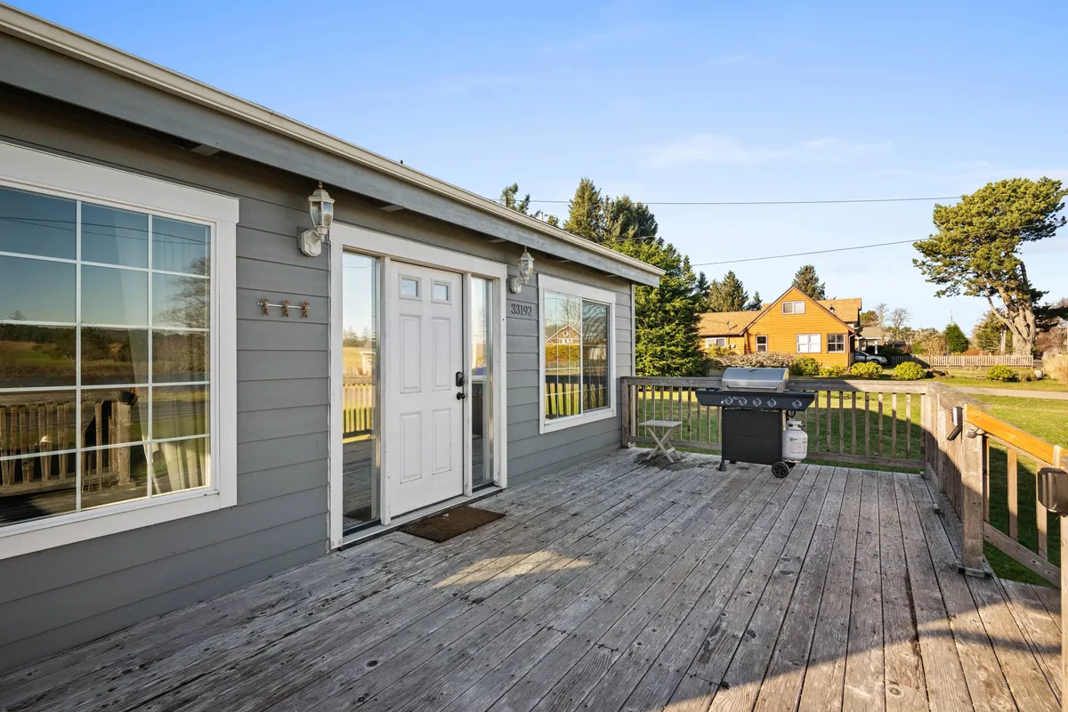 This image captures the exterior of the home, featuring the front door, a grill, a spacious deck area, and surrounding greenery. The scene suggests a welcoming space for outdoor dining and socializing, with enough room for family members of all ages to gather and enjoy the fresh air together.